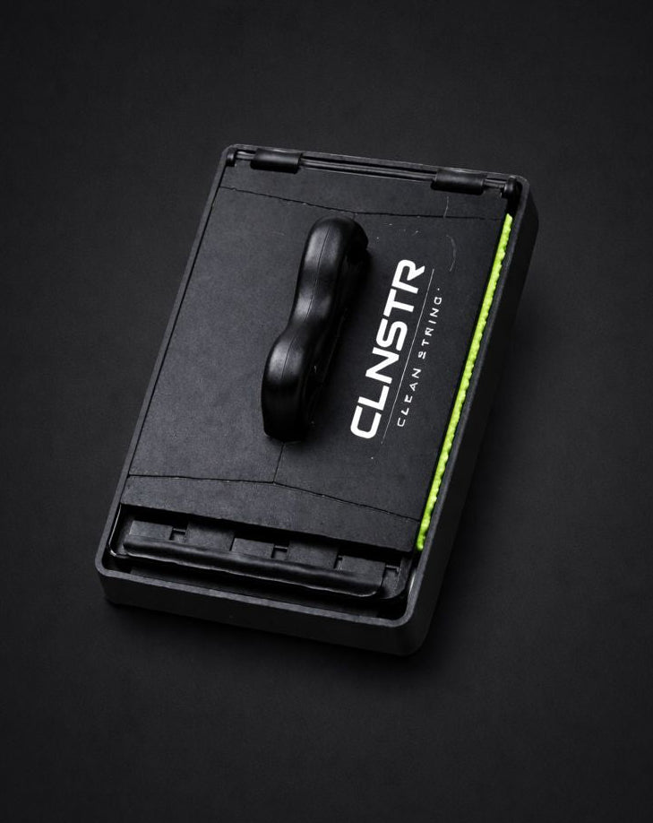 CLNSTR guitar string cleaner shown open on a black background, featuring a microfiber pad designed to clean guitar strings and extend string life