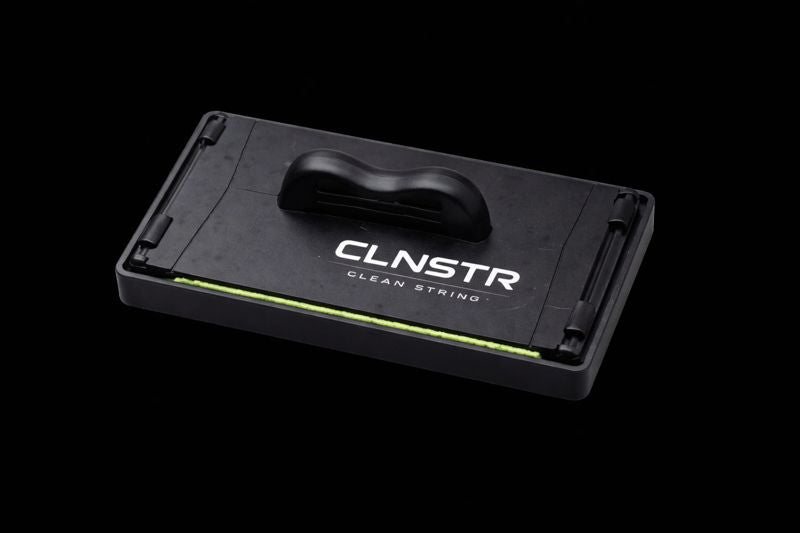 CLNSTR Clean String guitar string cleaner displayed horizontally on a black background, showing ergonomic grip and microfiber cleaning surface